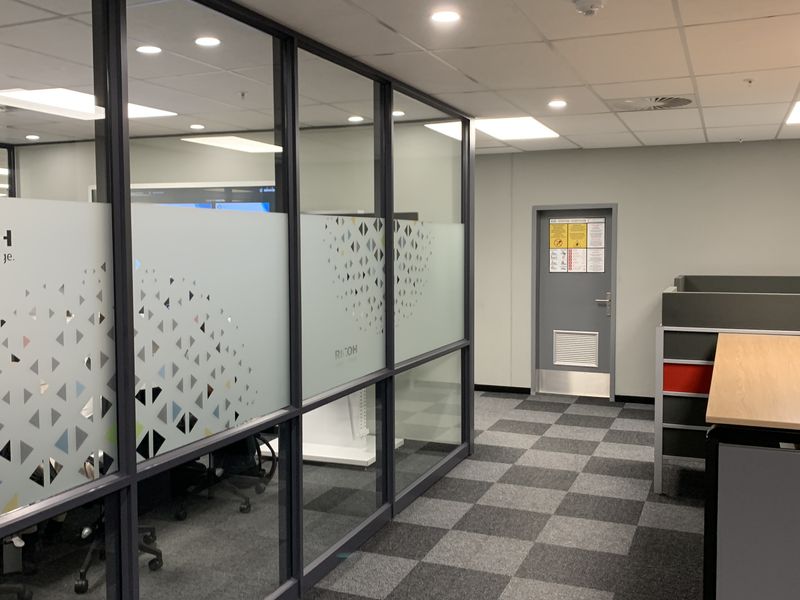 Modern office interior featuring glass partitioned meeting rooms, suspended ceilings with recessed lighting, and professional carpet tile flooring.