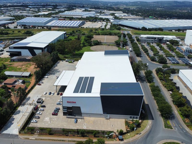 Aerial view of a modern industrial warehouse facility featuring a large roof with solar panels, dedicated parking, and a loading bay area.