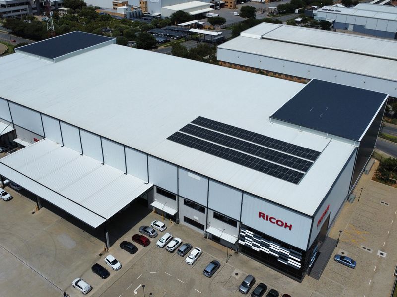 Aerial view of a large industrial warehouse facility featuring a metal roof with solar panels, loading docks, and an adjacent paved parking area.
