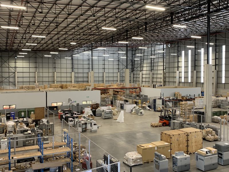 Spacious industrial warehouse featuring high ceilings with exposed steel trusses, concrete flooring, and integrated office partitions, suitable for logistics or manufacturing operations.