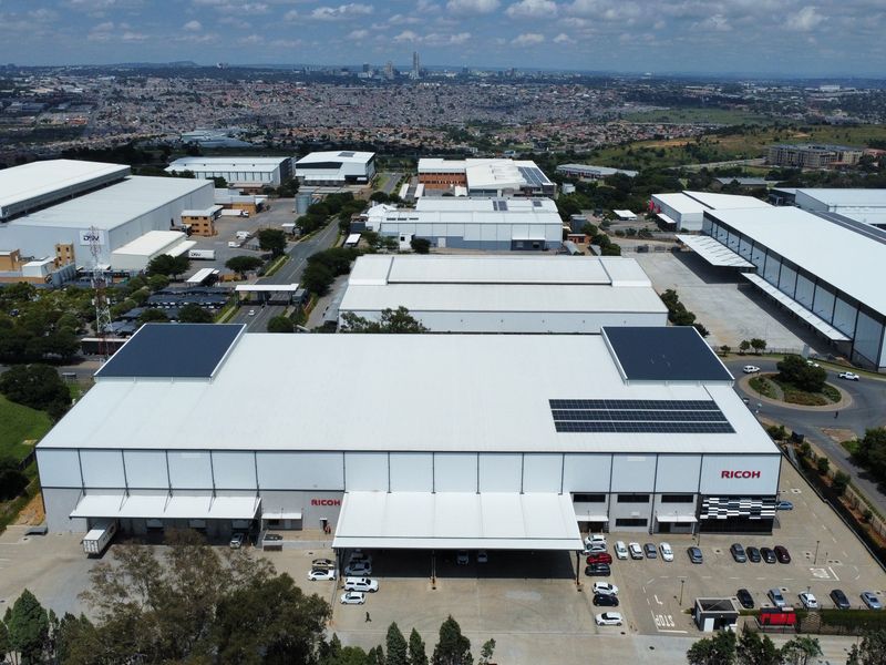 Aerial view of a large industrial warehouse facility featuring solar panels, extensive loading docks, and a paved parking area within a commercial business park.