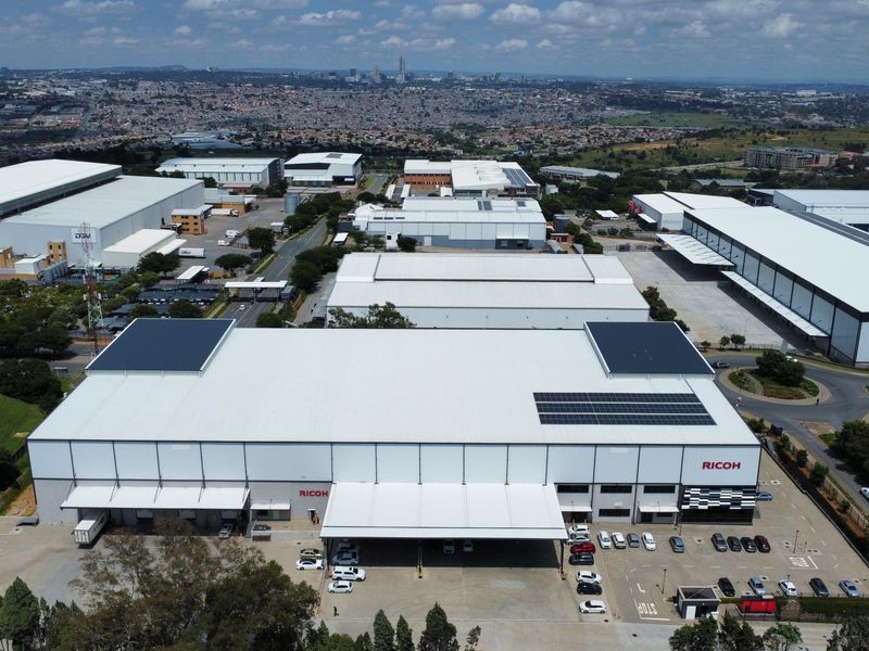 Aerial view of a large industrial warehouse facility featuring extensive loading bays, solar panel installations, and dedicated parking areas within a business park.