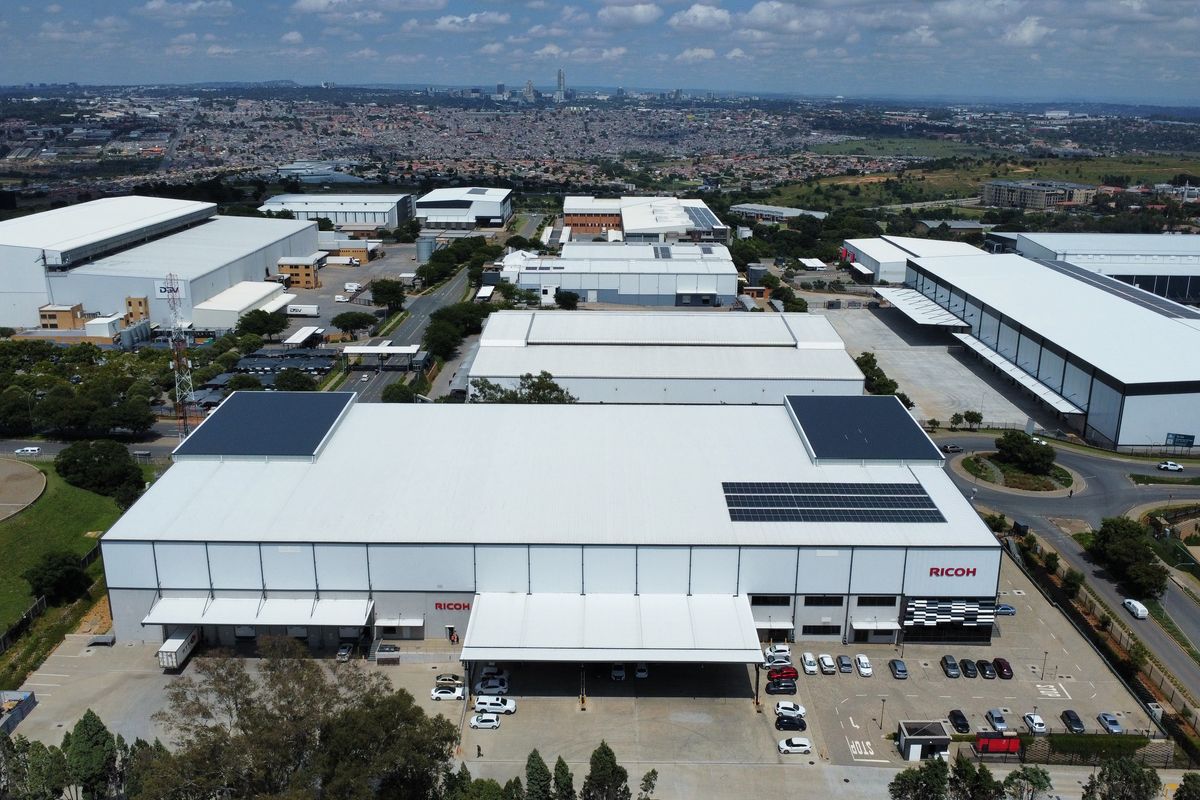 Aerial view of a large industrial warehouse facility featuring extensive loading bays, solar panel installations, and dedicated parking areas within a business park.