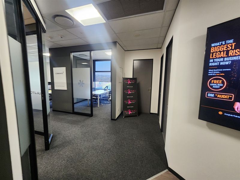 Modern office interior featuring glass partition walls, carpeted flooring, and recessed ceiling lighting, creating a professional and well-lit workspace environment.