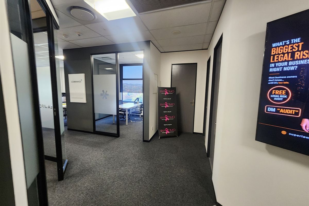 Modern office interior featuring glass partition walls, carpeted flooring, and recessed ceiling lighting, creating a professional and well-lit workspace environment.