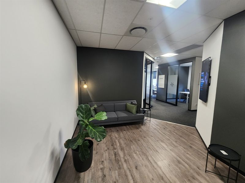 Modern office reception area featuring laminate flooring, glass partition walls, and a professional neutral color palette with recessed ceiling lighting.