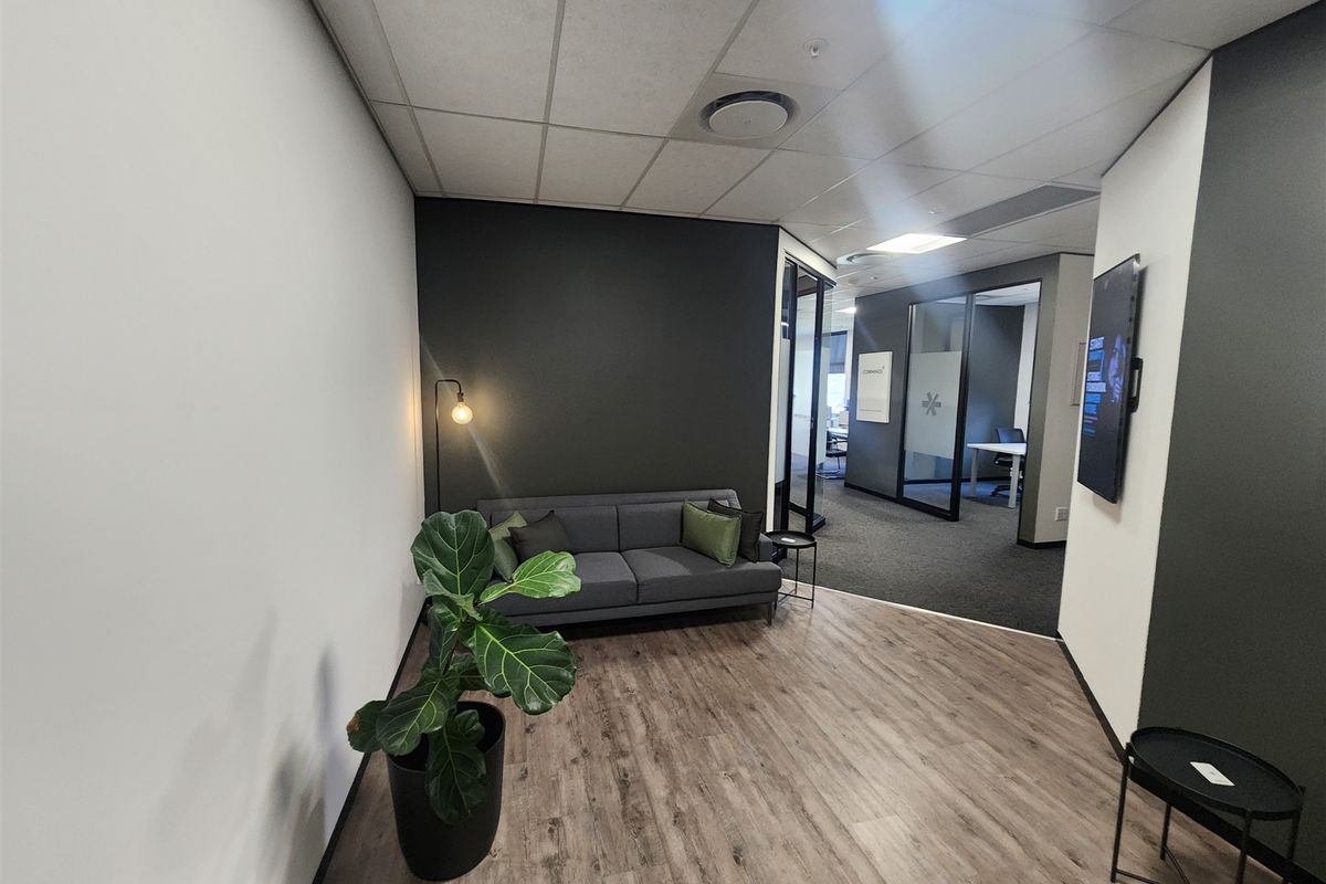 Modern office reception area featuring laminate flooring, glass partition walls, and a professional neutral color palette with recessed ceiling lighting.