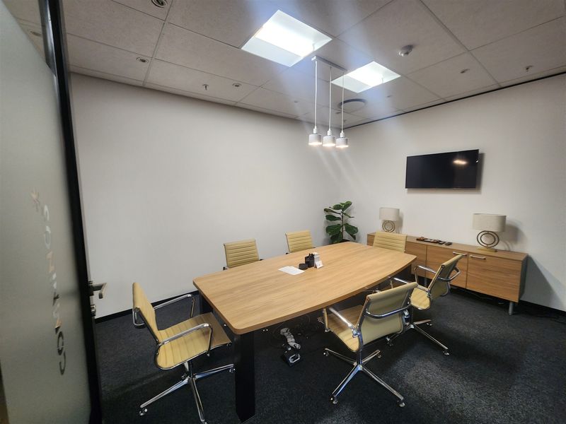 A professional meeting room featuring a suspended ceiling, recessed and pendant lighting, and carpeted flooring, providing a clean and functional workspace environment.