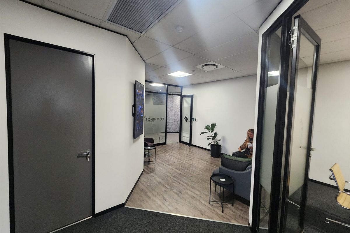 Modern office reception area featuring glass partitions, a mix of carpet and laminate flooring, and integrated ceiling lighting with air conditioning.