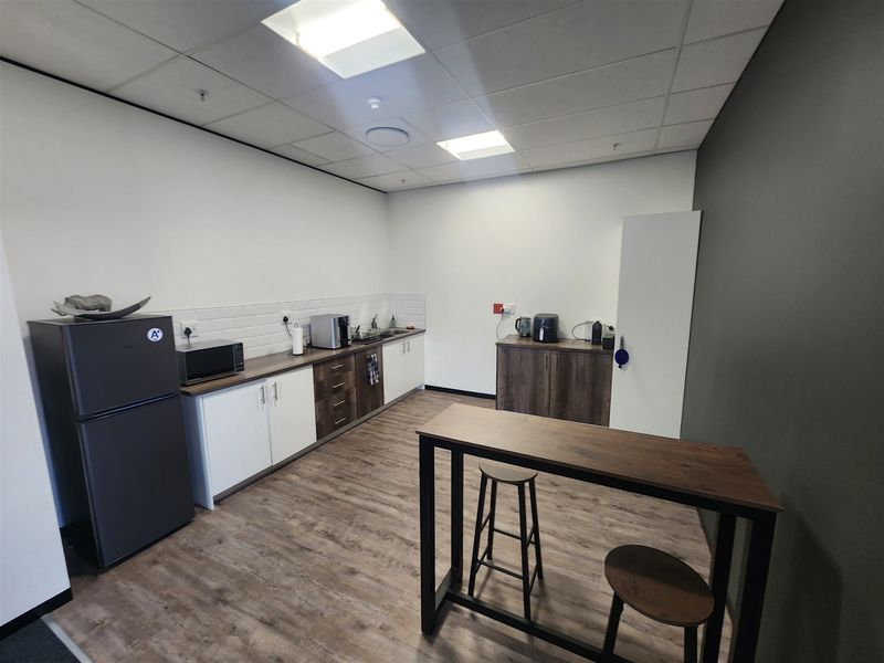 A modern office kitchenette featuring wood-look laminate flooring, built-in cabinetry with a subway tile backsplash, and a suspended ceiling with recessed lighting.