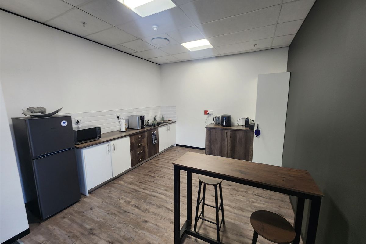 A modern office kitchenette featuring wood-look laminate flooring, built-in cabinetry with a subway tile backsplash, and a suspended ceiling with recessed lighting.