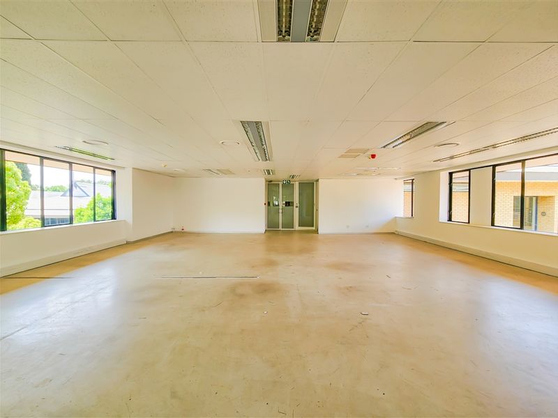 A spacious, vacant open-plan office area featuring a suspended ceiling, recessed lighting, and large windows providing ample natural light.