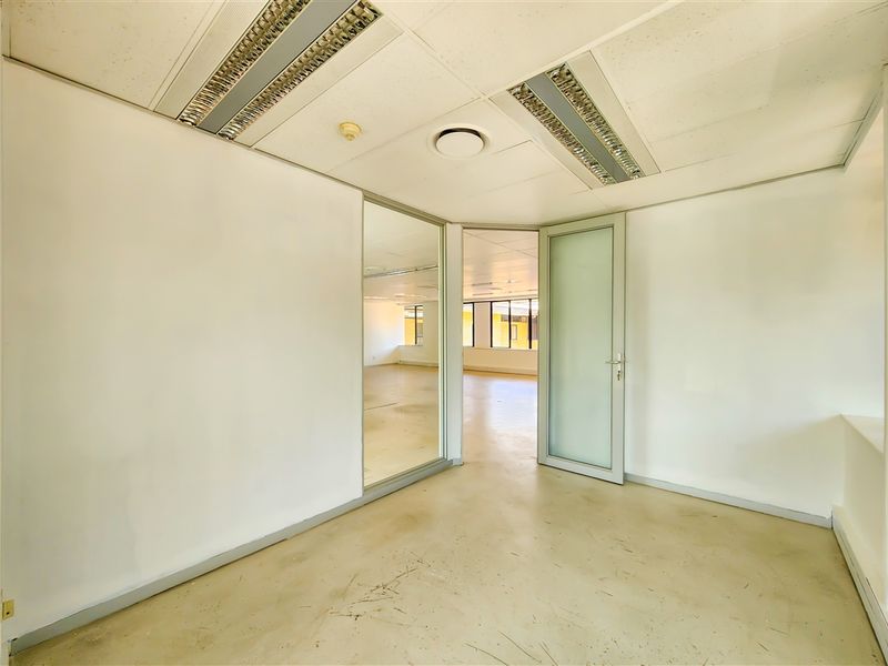 An empty office space featuring a suspended ceiling with recessed lighting, a glass partition, and a frosted glass door, offering a clean, professional layout.
