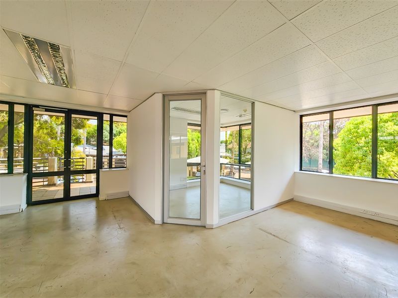 A bright, vacant office space featuring large windows, glass partitioning, suspended ceilings, and durable concrete flooring, offering a clean canvas for professional use.