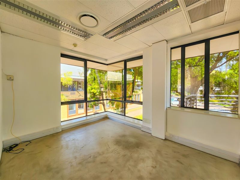 A bright, vacant office space featuring large corner windows, suspended ceilings with recessed lighting, and exposed concrete flooring, offering a clean canvas for customization.