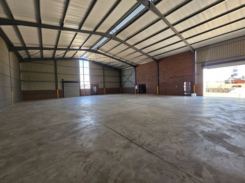 Spacious industrial warehouse featuring high ceilings, exposed brickwork, concrete flooring, and large roller shutter door access.