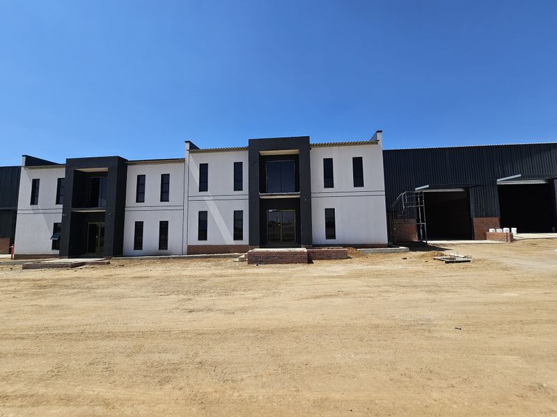 Modern industrial facility featuring a multi-story office facade with large windows and adjacent warehouse space under construction.