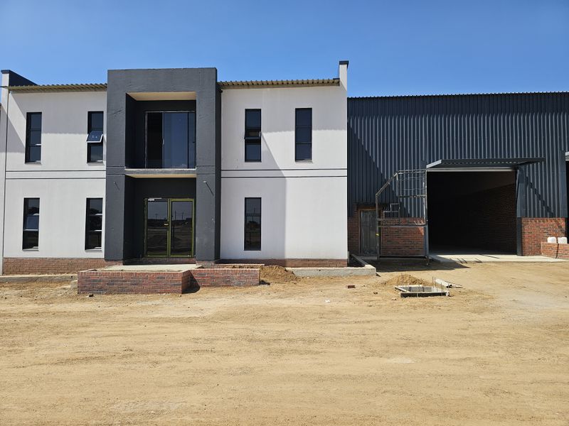 Modern industrial facility featuring a two-story office block with a large attached warehouse, currently undergoing final exterior site completion.
