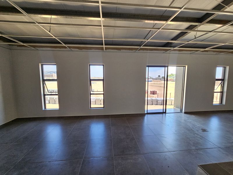 An open-plan industrial space featuring large format floor tiles, multiple windows, and an exposed ceiling grid ready for final installation.
