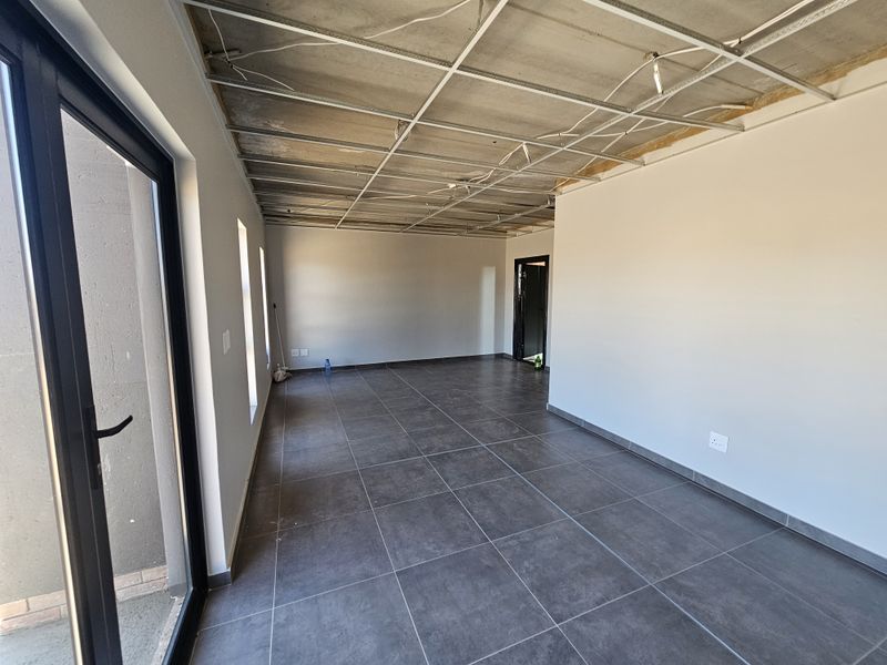An unfinished interior space featuring large format floor tiles, black framed glass doors, and an exposed ceiling grid ready for final installation.