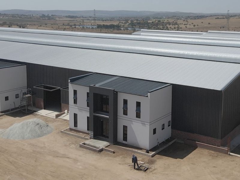Aerial view of a modern industrial warehouse complex featuring large metal-clad structures and integrated office blocks under construction.