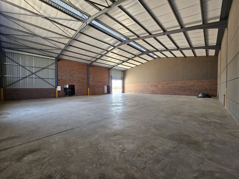 Spacious industrial warehouse featuring high ceilings, exposed brick walls, polished concrete flooring, and large roller door access.