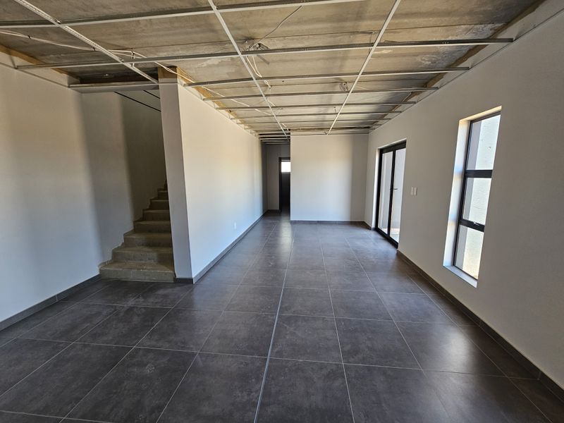 An unfinished open-plan industrial space featuring dark floor tiles, large windows, and an exposed ceiling grid ready for final fit-out.