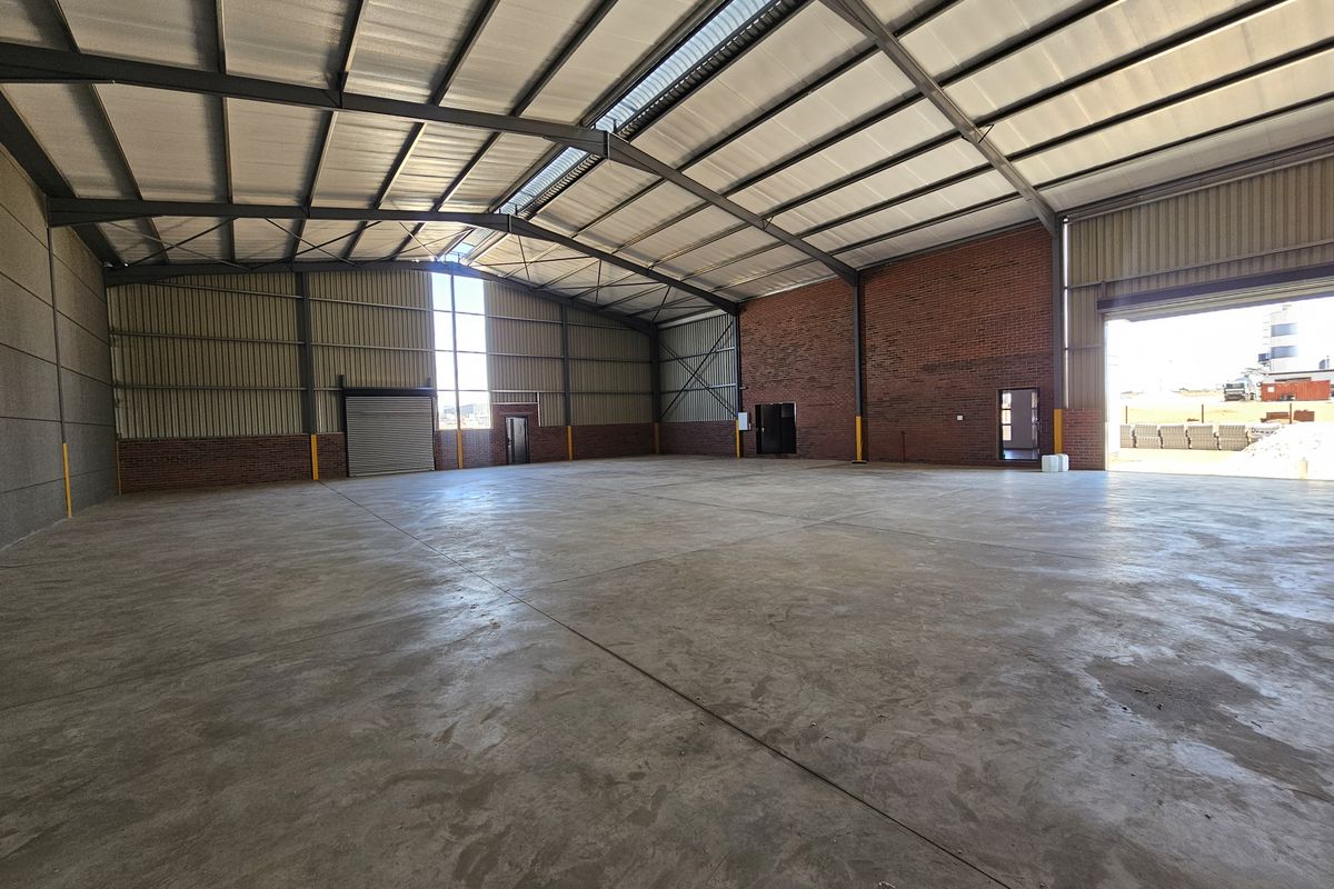 Spacious industrial warehouse featuring high ceilings, exposed brickwork, concrete flooring, and large roller shutter door access.
