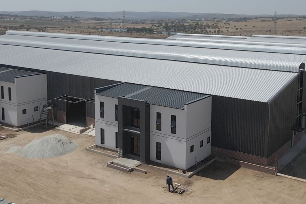 Aerial view of a modern industrial warehouse complex featuring large metal-clad structures and integrated office blocks under construction.