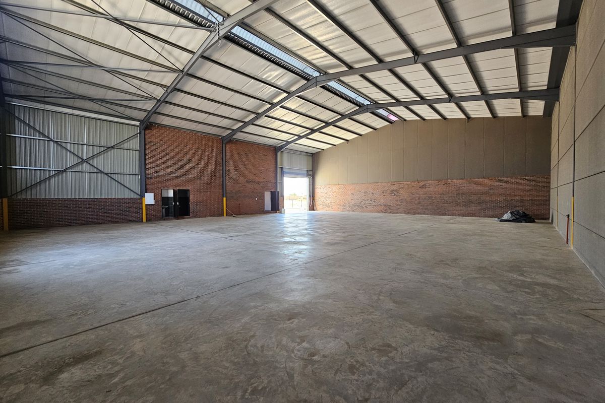 Spacious industrial warehouse featuring high ceilings, exposed brick walls, polished concrete flooring, and large roller door access.