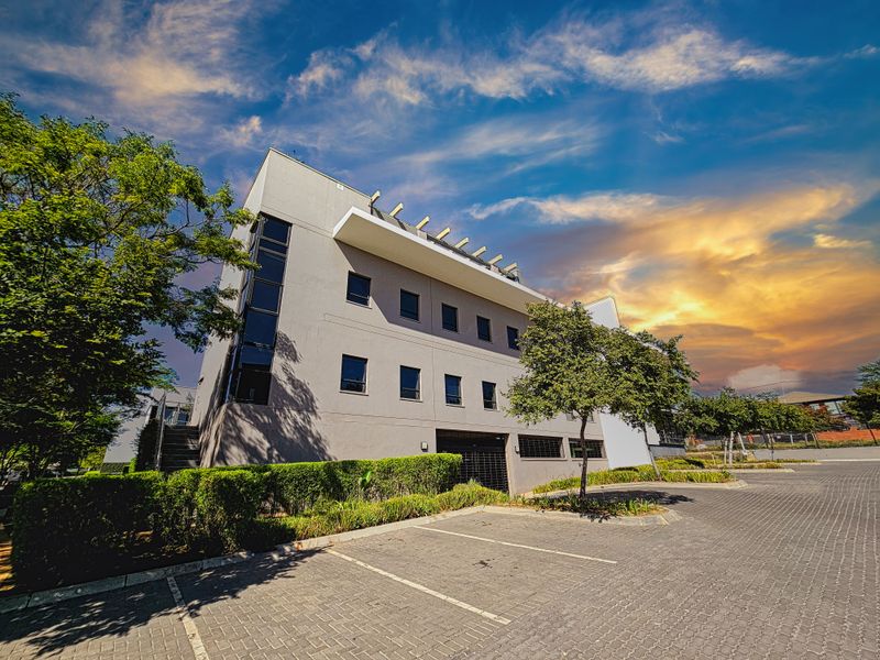 A professional exterior view of a multi-story office building featuring a paved parking area and well-maintained landscaped hedging.