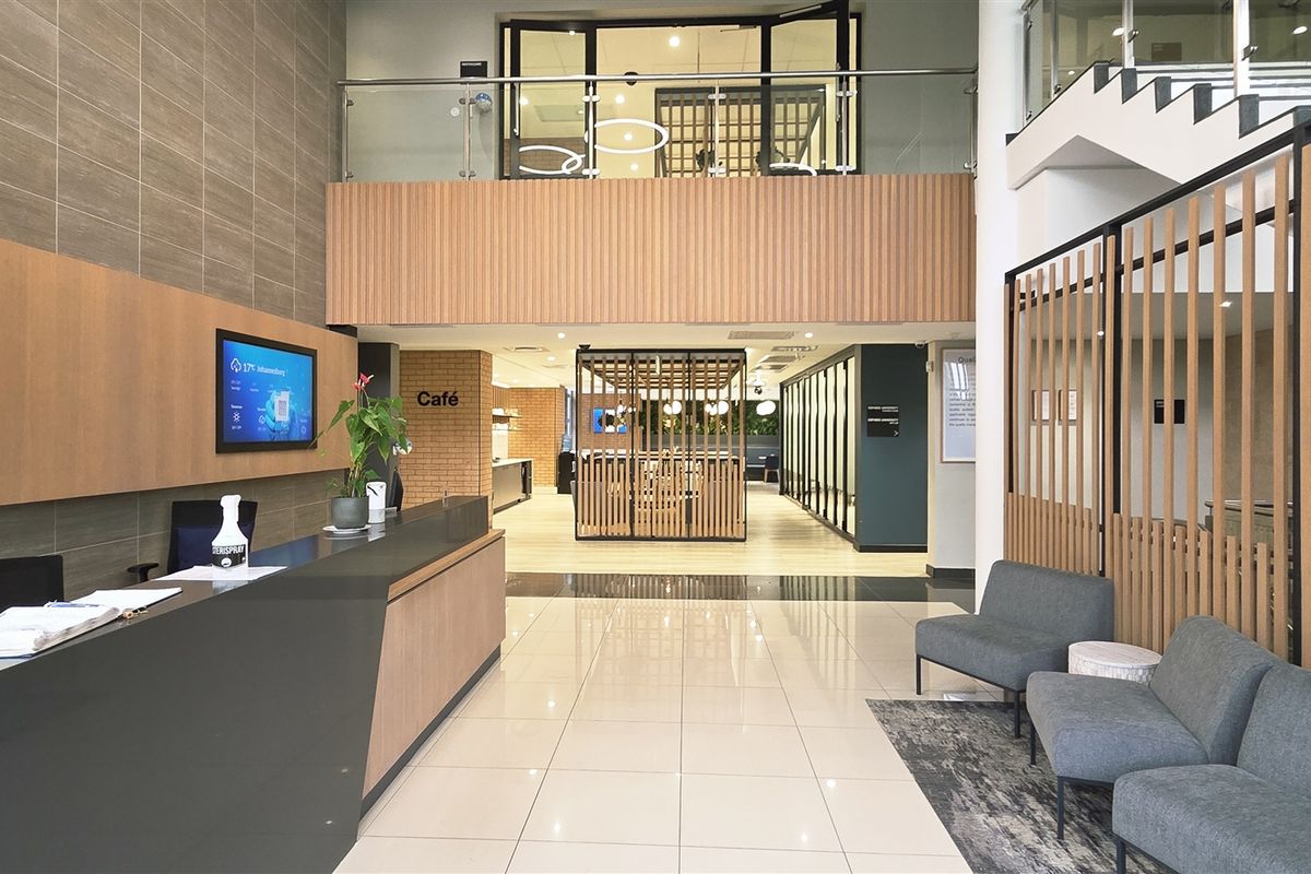 Modern office reception area featuring a sleek reception desk, tiled flooring, and a feature staircase with timber slat detailing and glass balustrades.