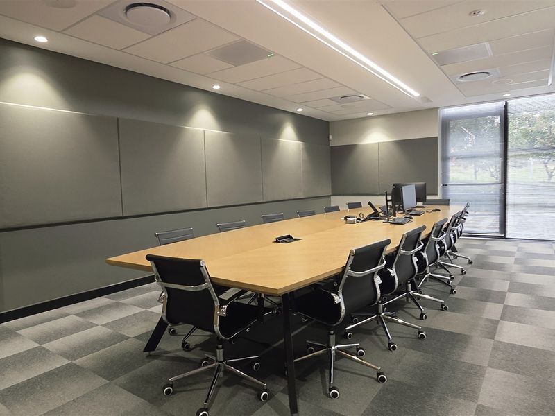 Modern professional boardroom featuring acoustic wall paneling, recessed lighting, suspended ceiling, and large windows with integrated blinds.
