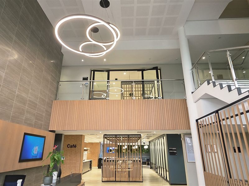 Modern double-volume office entrance lobby featuring contemporary pendant lighting, a glass balustrade staircase, and elegant timber slat wall paneling.