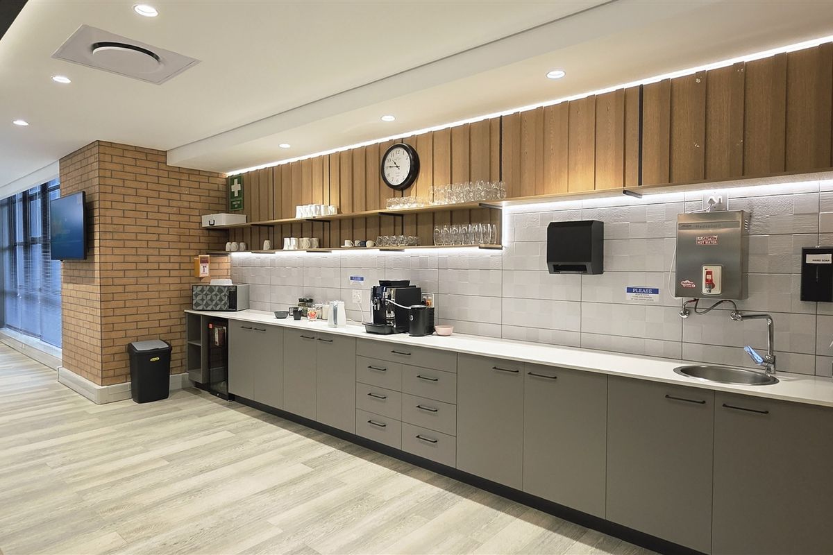 Modern office kitchenette featuring sleek cabinetry, wood slat wall accents, exposed brick detailing, and a built-in hot water dispenser.