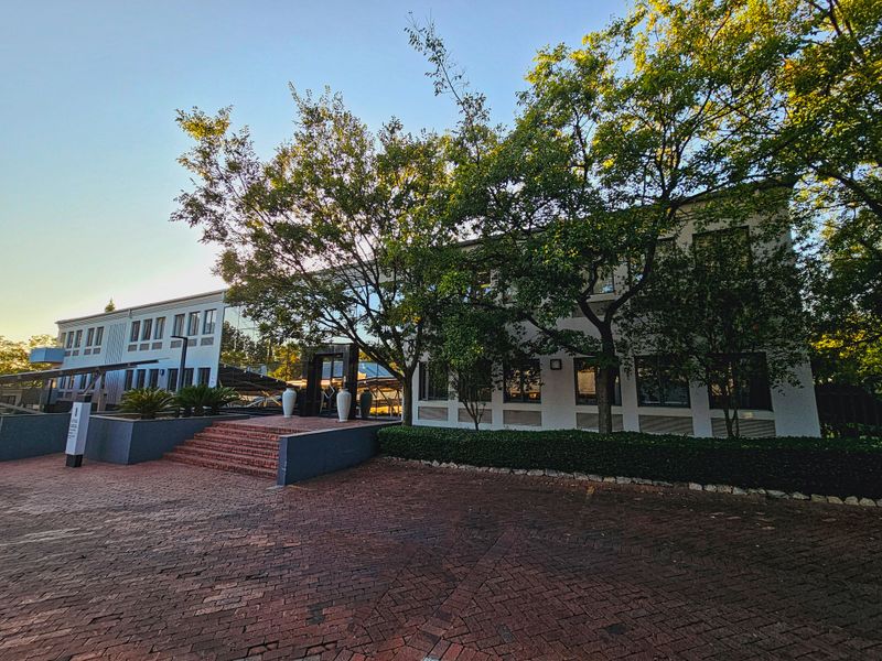 Front exterior view of a professional office building featuring a brick paved entrance, glass facade, and mature trees.