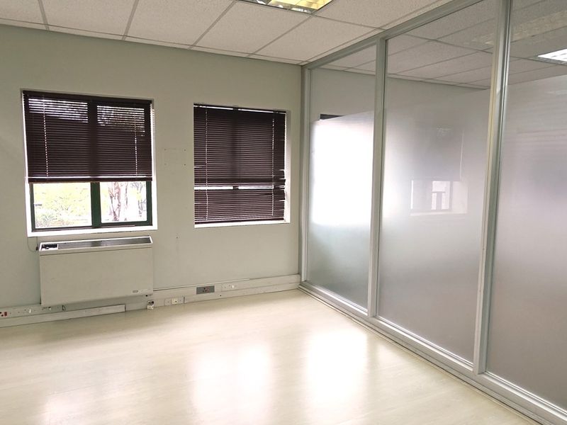 A bright, empty office space featuring glass partition walls, suspended ceilings, recessed lighting, and an integrated HVAC unit.