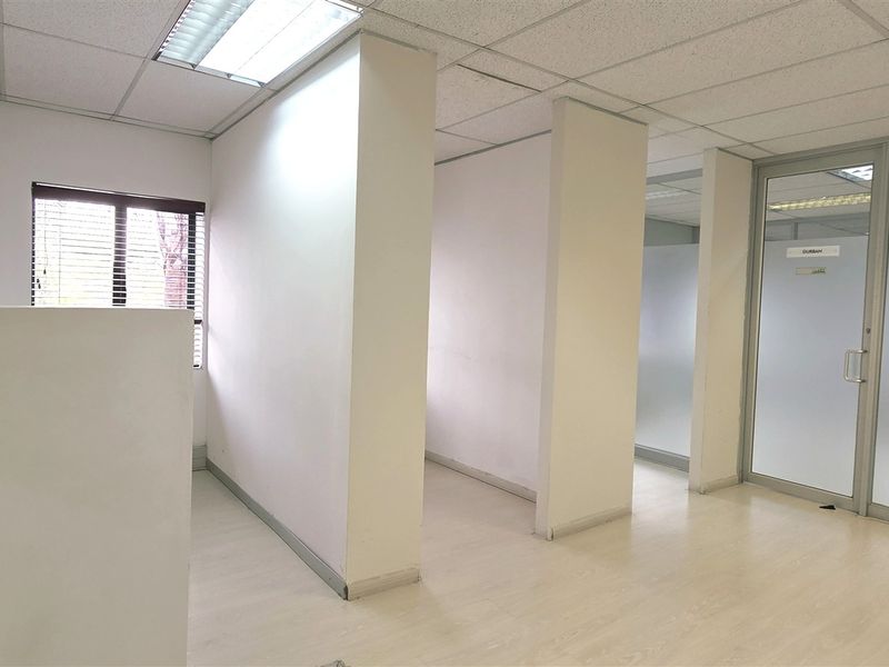 A bright, vacant office space featuring glass partitions, suspended ceilings with recessed lighting, and light-toned laminate flooring, offering a clean and professional work environment.