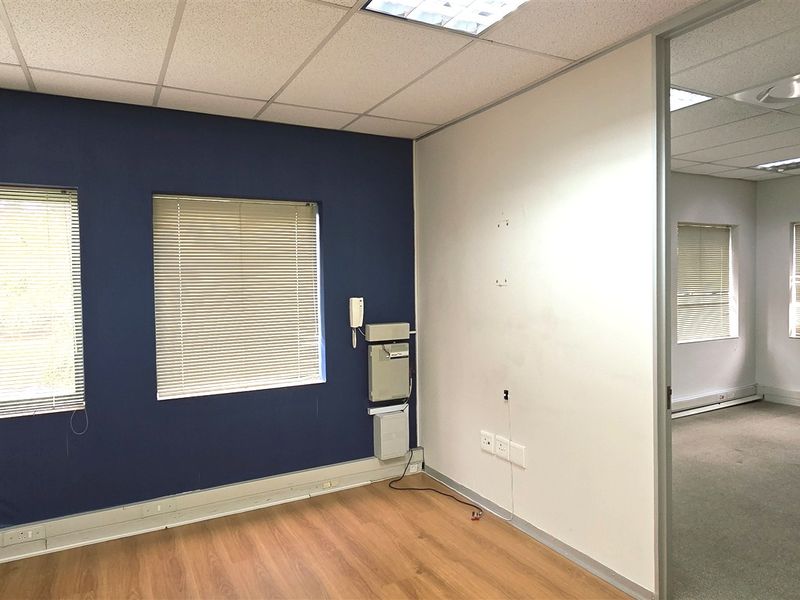 Empty office space featuring laminate and carpet flooring, suspended ceilings with recessed lighting, and a sliding door connecting to an adjacent office area.