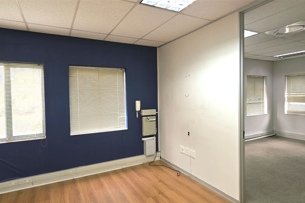 Empty office space featuring laminate and carpet flooring, suspended ceilings with recessed lighting, and a sliding door connecting to an adjacent office area.