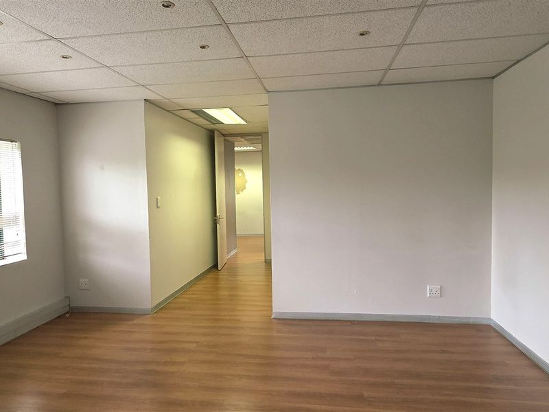 A bright, empty office space featuring laminate flooring, a suspended ceiling with recessed lighting, and neutral walls, offering a clean and versatile workspace.