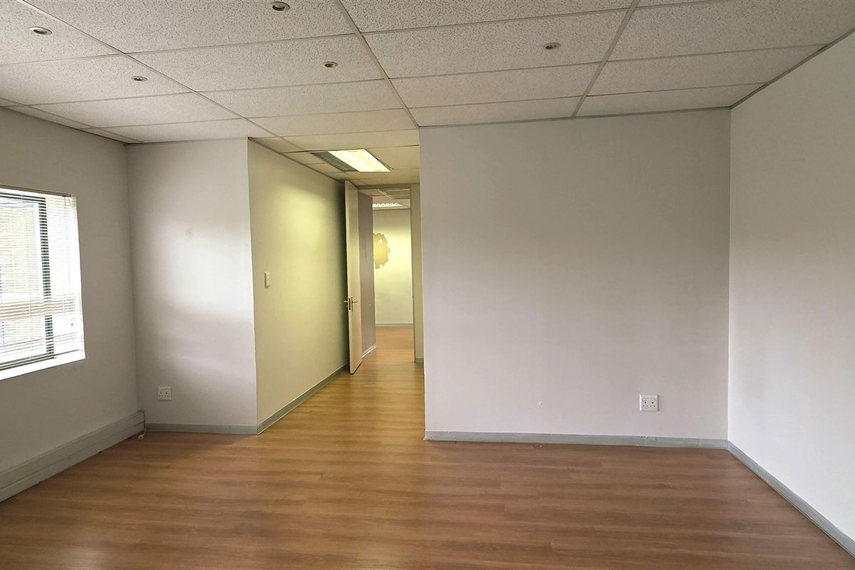 A bright, empty office space featuring laminate flooring, a suspended ceiling with recessed lighting, and neutral walls, offering a clean and versatile workspace.