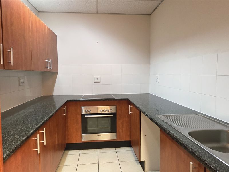 A functional office kitchen featuring wood-finish cabinetry, granite countertops, a stainless steel sink, and a built-in oven with an electric cooktop.