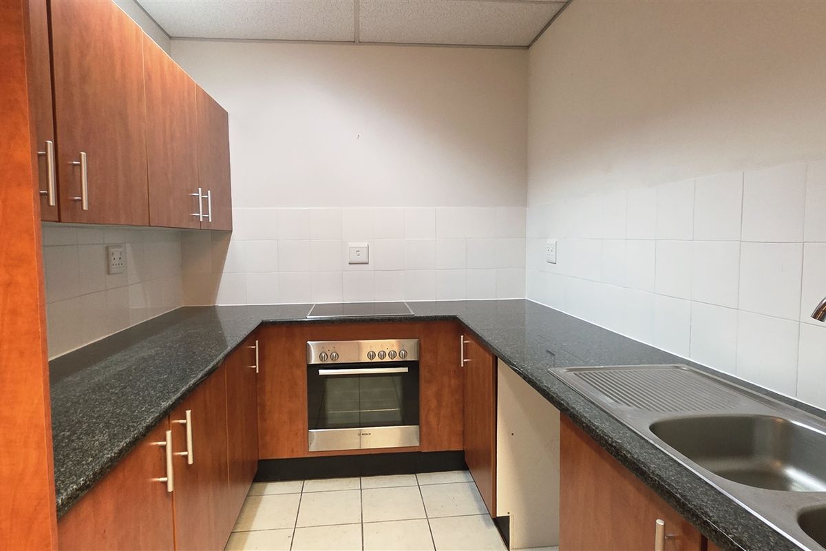 A functional office kitchen featuring wood-finish cabinetry, granite countertops, a stainless steel sink, and a built-in oven with an electric cooktop.