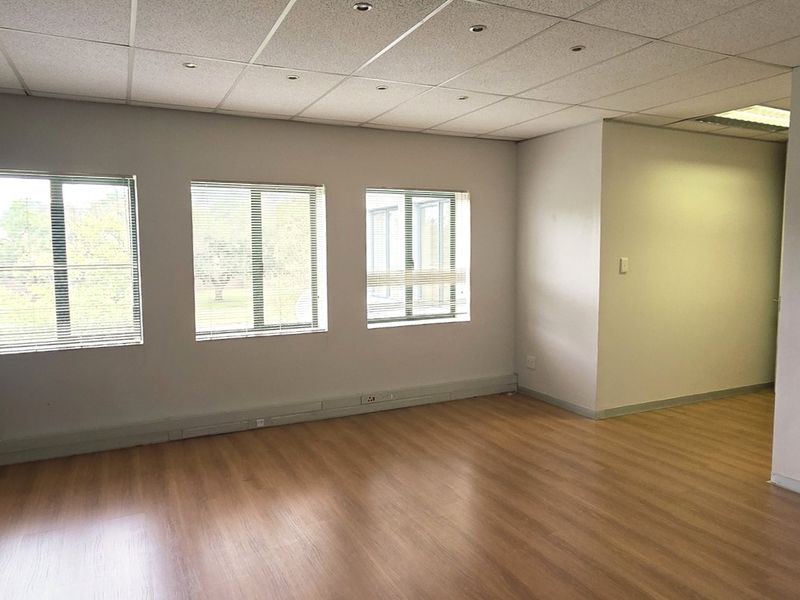 A bright, vacant office space featuring laminate flooring, recessed lighting, and large windows with blinds, offering a clean and professional work environment.