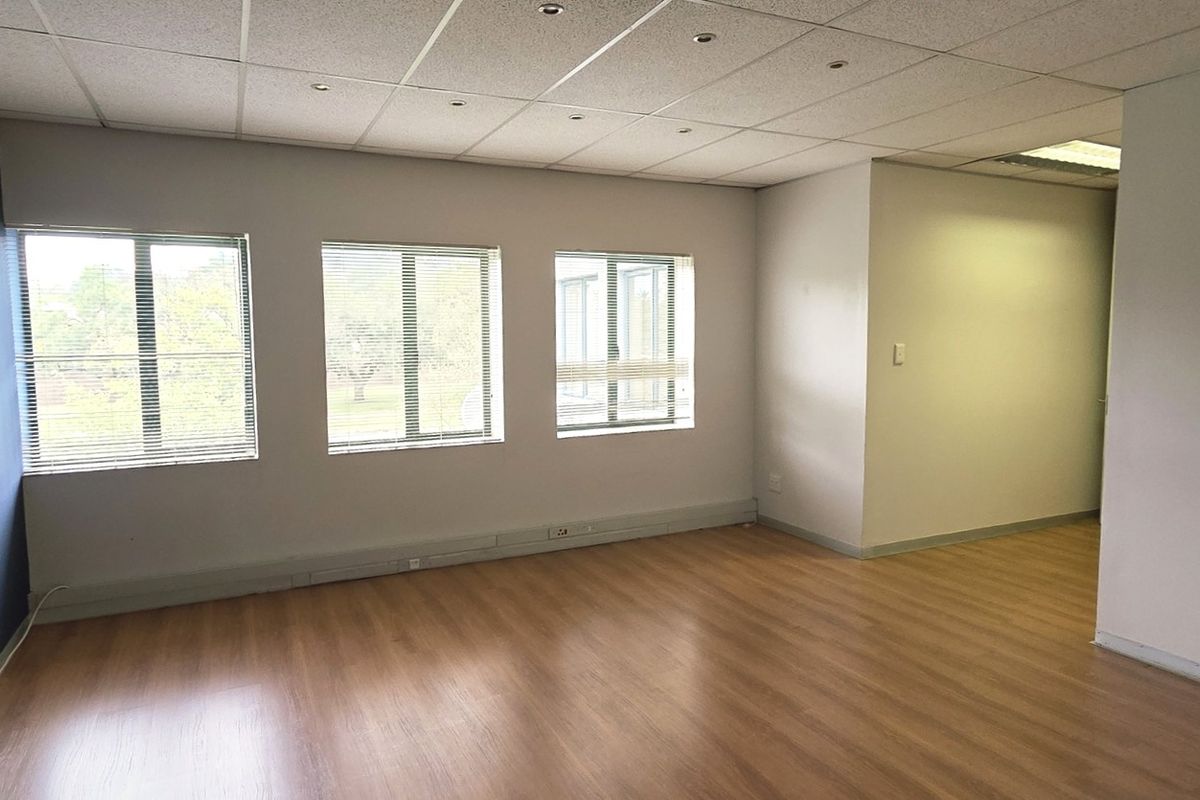 A bright, vacant office space featuring laminate flooring, recessed lighting, and large windows with blinds, offering a clean and professional work environment.