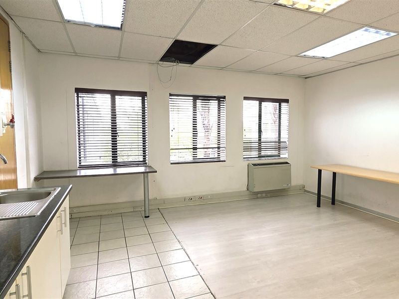 An open-plan office space featuring a kitchenette, tiled flooring, air conditioning, and large windows with blinds. Requires minor ceiling and wall repairs.