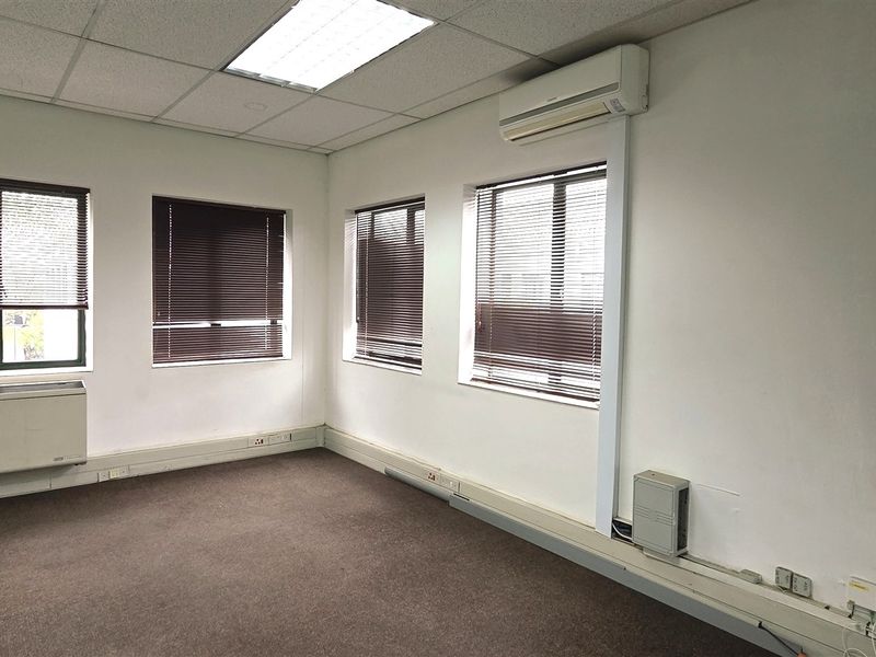 A vacant office space featuring carpet flooring, suspended ceilings, recessed lighting, split-system air conditioning, and large windows with venetian blinds.