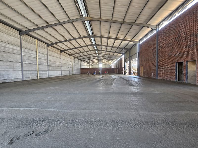Large industrial warehouse space featuring a steel portal frame, exposed brickwork, precast concrete wall panels, and a freshly laid concrete floor.