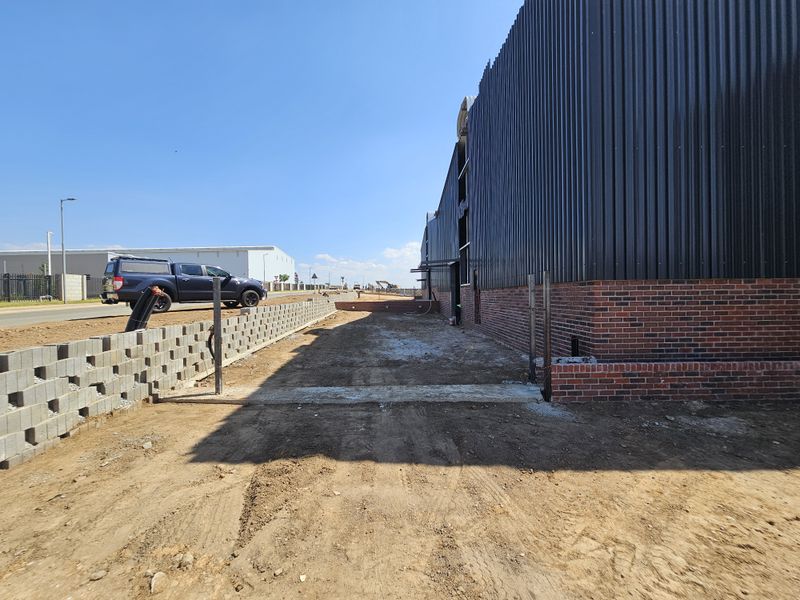 Exterior view of an industrial property under construction, featuring corrugated metal cladding, face brick base, and an unfinished ground area.